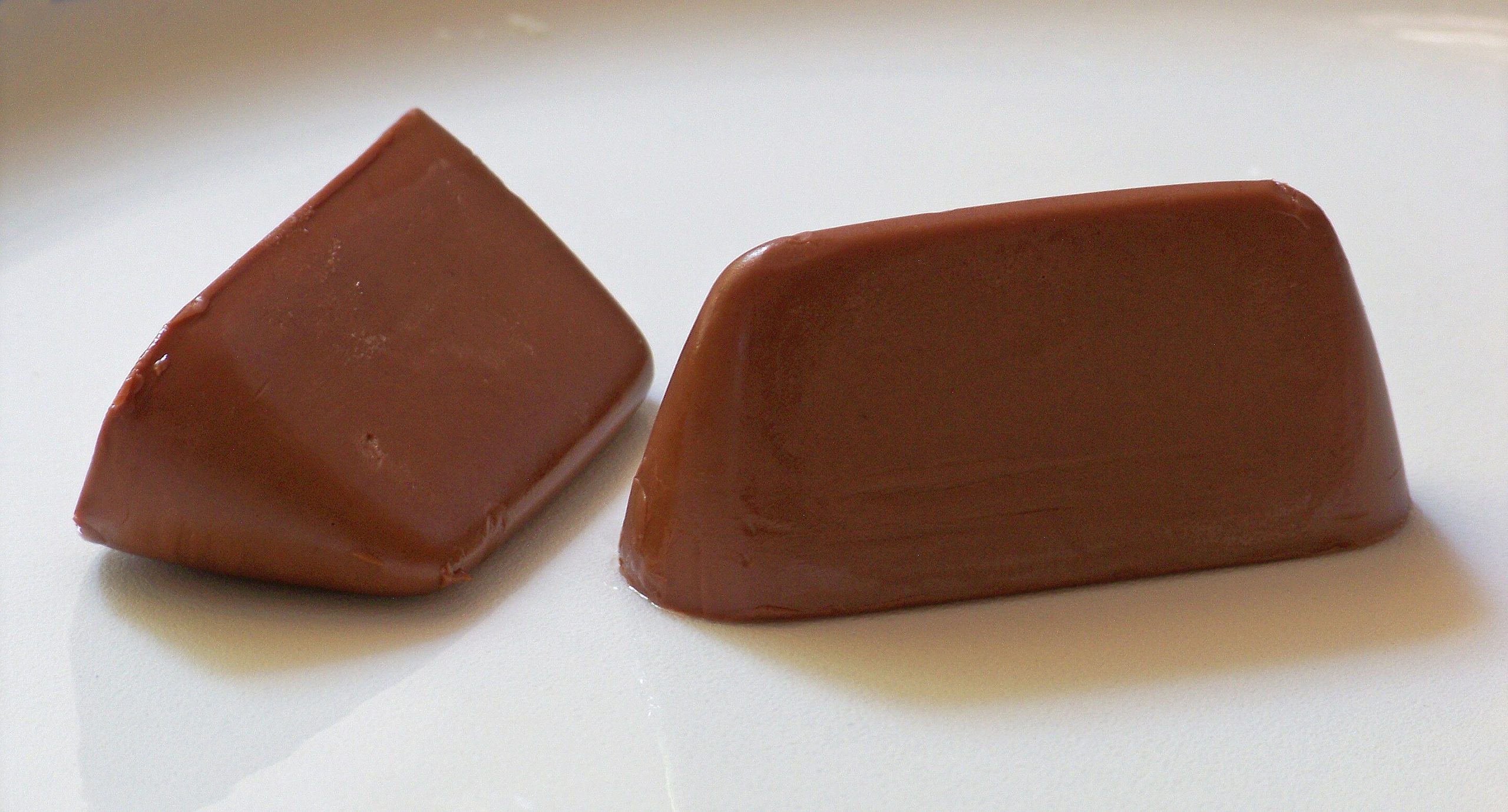 two triangular pieces of smooth chocolate placed on a white plate showcasing their shiny rich brown surface with soft edges digital production Two triangular pieces of smooth chocolate placed on a white plate, showcasing their shiny, rich brown surface with soft edges.