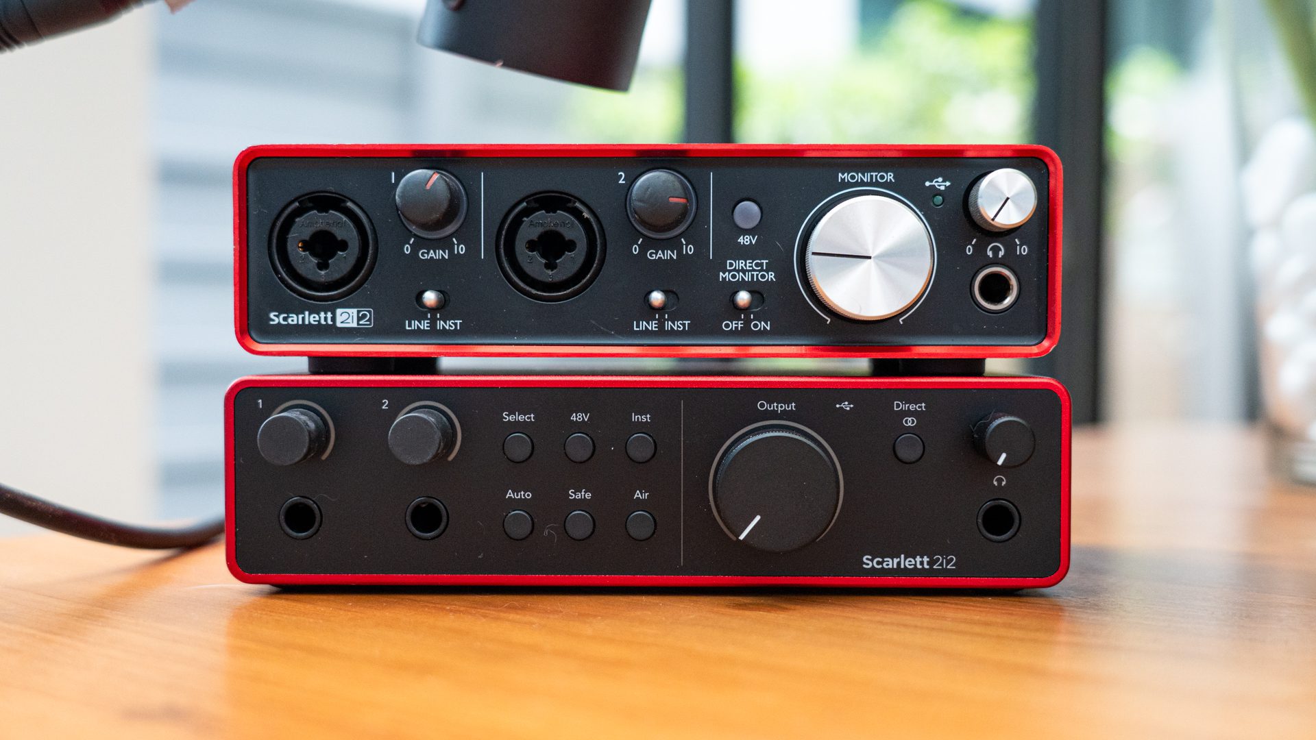 a closeup view of two audio interfaces the scarlett 2i2 and scarlett 2i2 stacked on a wooden table the top interface features xlr inputs gain knobs and a monitor control while the bottom has output controls and multiple buttons digital production A close-up view of two audio interfaces, the Scarlett 2i2 and Scarlett 2i2, stacked on a wooden table. The top interface features XLR inputs, gain knobs, and a monitor control, while the bottom has output controls and multiple buttons.