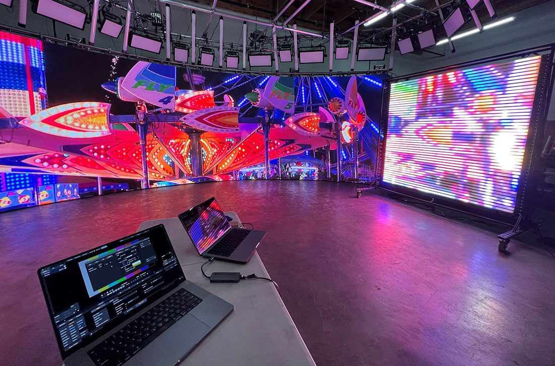 a modern production studio showcasing colorful led screens with vibrant patterns a laptop displaying control software is on the foreground table with more screens illuminating the space with bright light effects digital production A modern production studio showcasing colorful LED screens with vibrant patterns. A laptop displaying control software is on the foreground table, with more screens illuminating the space with bright light effects.