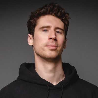 a young man with curly hair wearing a black hoodie looking confidently at the camera against a dark gray background the lighting emphasizes his facial features digital production A young man with curly hair wearing a black hoodie, looking confidently at the camera against a dark gray background. The lighting emphasizes his facial features.