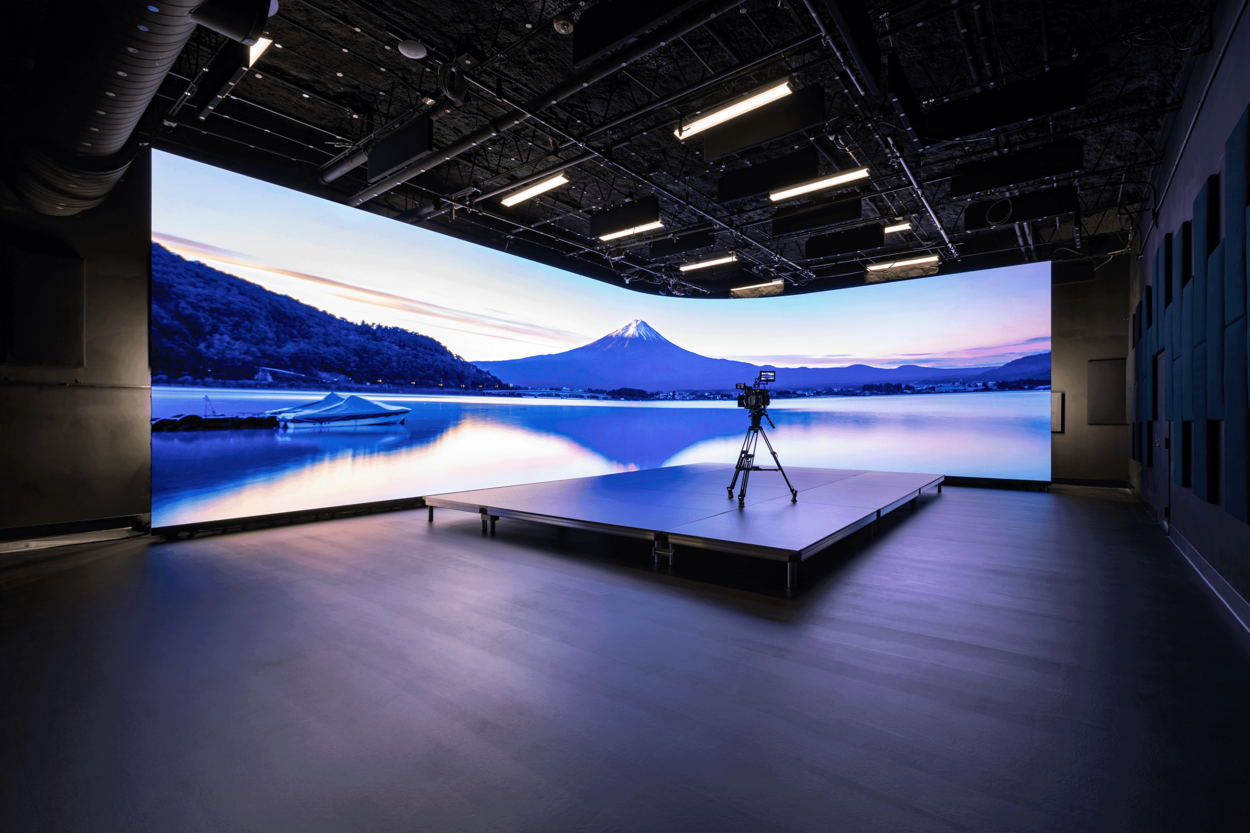 a hightech studio featuring a large display of a serene landscape with a mountain and water a camera is positioned on a platform in the foreground highlighting the modern production setup digital production A high-tech studio featuring a large display of a serene landscape with a mountain and water. A camera is positioned on a platform in the foreground, highlighting the modern production setup.