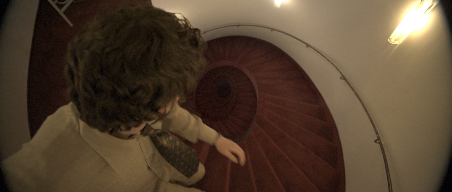 a person with curly hair dressed in a lightcolored outfit descends a spiral staircase the staircase features wooden steps and is illuminated by soft lighting along the walls creating a warm atmosphere digital production A person with curly hair dressed in a light-colored outfit descends a spiral staircase. The staircase features wooden steps and is illuminated by soft lighting along the walls, creating a warm atmosphere.