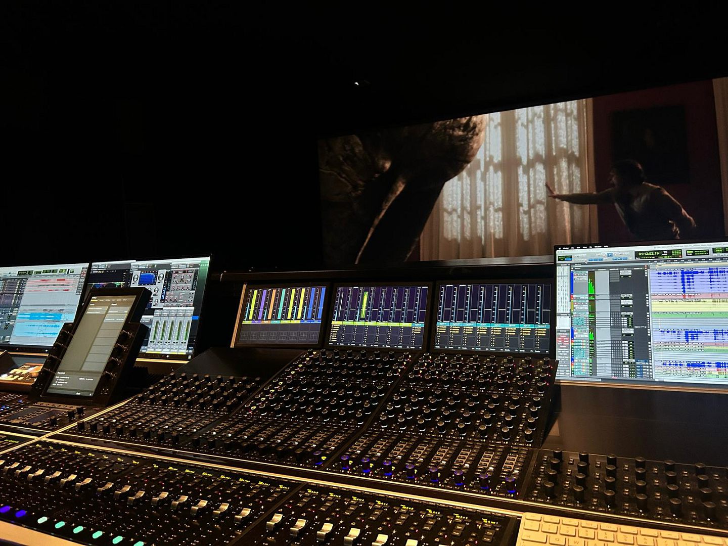 a modern sound studio showcasing an intricate mixing console with numerous dials and screens displaying audio waveforms in the background a large screen features a scene from a film highlighting the creative environment digital production A modern sound studio showcasing an intricate mixing console with numerous dials and screens displaying audio waveforms. In the background, a large screen features a scene from a film, highlighting the creative environment.