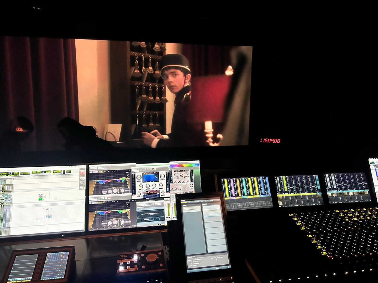 a sound mixing studio displaying various digital audio equipment and mixing consoles with a film scene shown on a large screen in the background featuring a man in a hat sitting and looking at something digital production A sound mixing studio displaying various digital audio equipment and mixing consoles, with a film scene shown on a large screen in the background featuring a man in a hat, sitting and looking at something.
