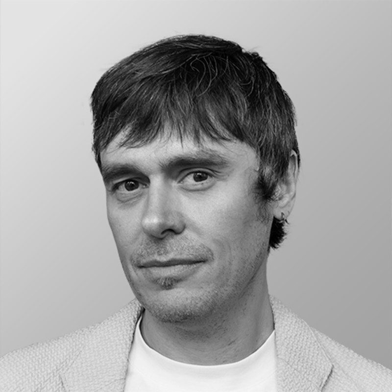 a closeup portrait of a man with short tousled hair wearing a lightcolored blazer over a white shirt he has a slight smile and is facing slightly to the left against a gradient gray backdrop digital production A close-up portrait of a man with short, tousled hair, wearing a light-colored blazer over a white shirt. He has a slight smile and is facing slightly to the left against a gradient gray backdrop.