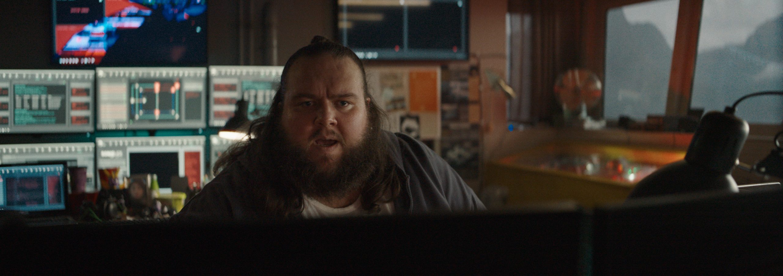 a man with long hair and a beard looking surprised while seated in front of multiple computer monitors displaying various data and graphics in a dimly lit control room digital production A man with long hair and a beard, looking surprised while seated in front of multiple computer monitors displaying various data and graphics in a dimly lit control room.