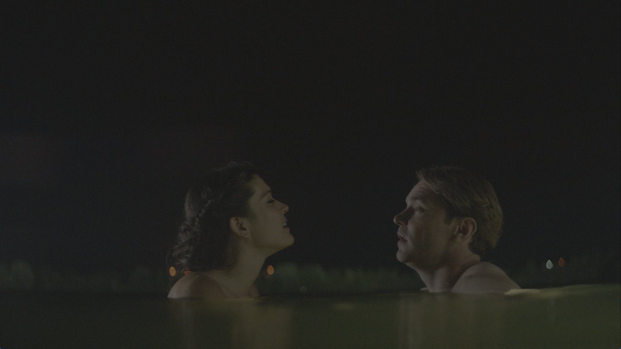 a man and a woman are partially submerged in water at night facing each other the scene is illuminated by soft ambient light highlighting their expressions in a quiet intimate moment digital production A man and a woman are partially submerged in water at night, facing each other. The scene is illuminated by soft ambient light, highlighting their expressions in a quiet, intimate moment.