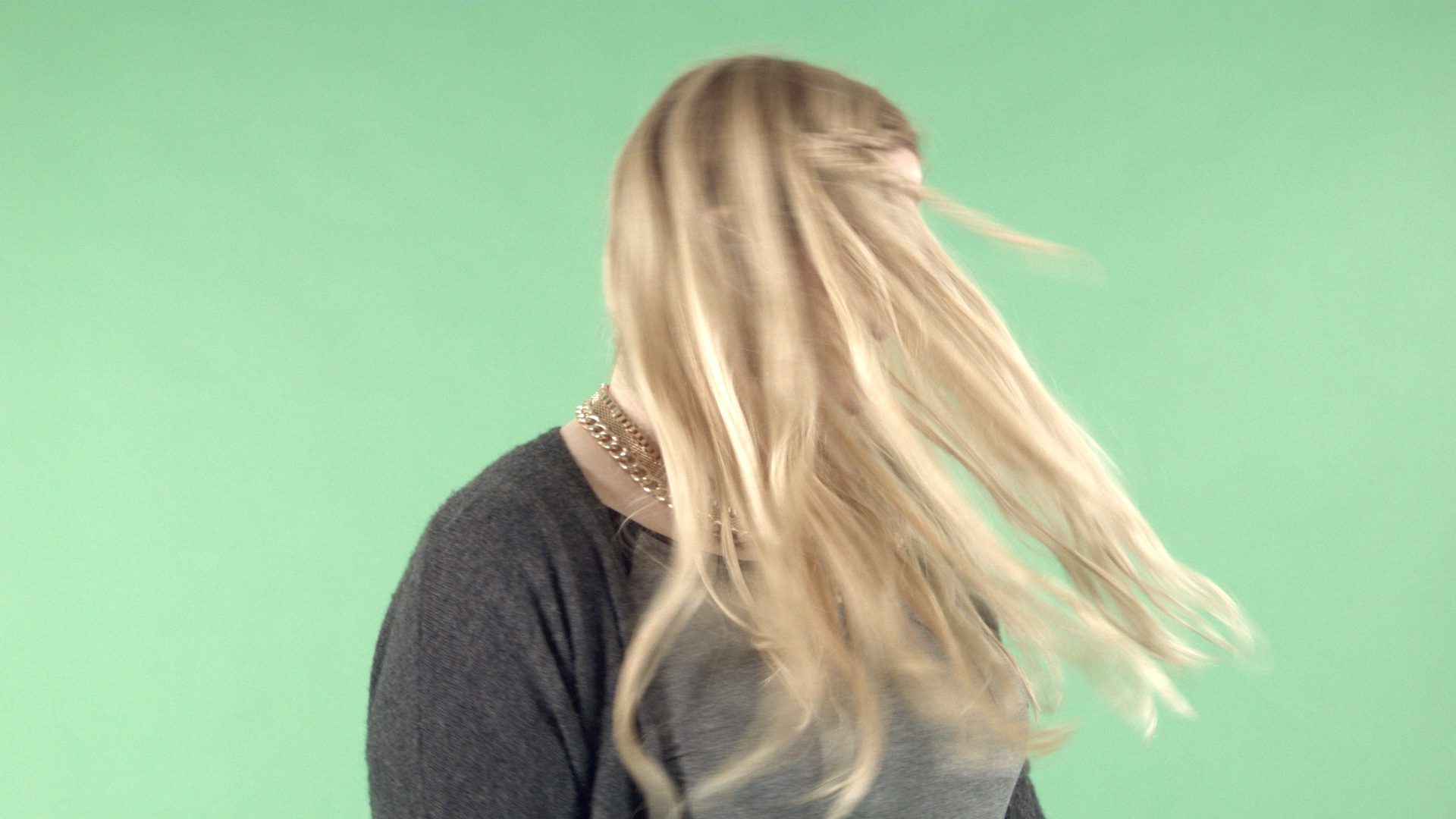 a woman with long flowing blonde hair is in motion turning her head as her hair cascades around her she is wearing a dark gray sweater with a green screen background enhancing the lively scene digital production A woman with long, flowing blonde hair is in motion, turning her head as her hair cascades around her. She is wearing a dark gray sweater, with a green screen background enhancing the lively scene.