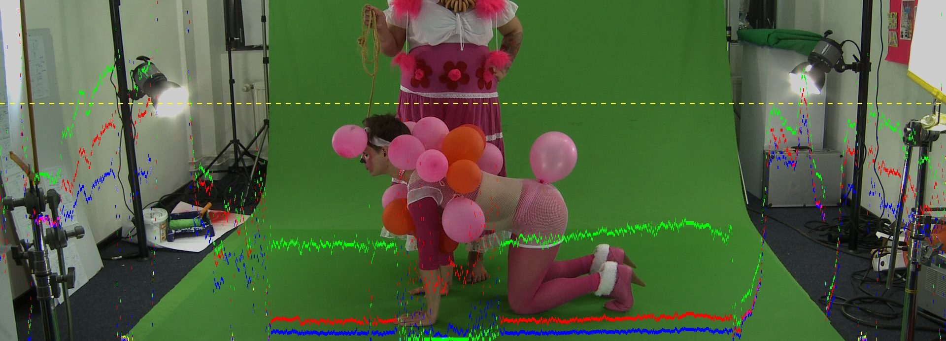 two performers in playful costumes set against a green screen backdrop one is wearing a colorful outfit with balloon accessories while the other is on all fours decorated with balloons in a lighthearted scene digital production Two performers in playful costumes set against a green screen backdrop. One is wearing a colorful outfit with balloon accessories while the other is on all fours, decorated with balloons, in a lighthearted scene.