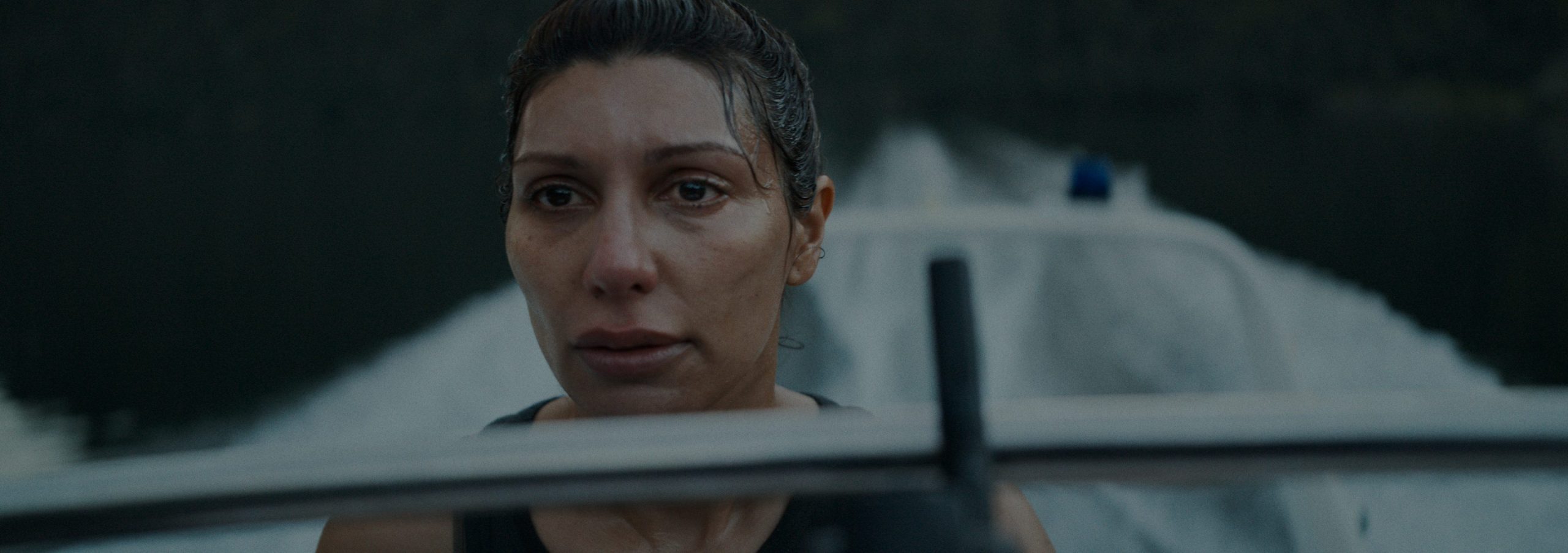 a closeup of a woman on a boat looking intently ahead her hair is wet and water glistens on her skin as she focuses on the environment around her with a blurred boat in the background cutting through calm water digital production A close-up of a woman on a boat, looking intently ahead. Her hair is wet, and water glistens on her skin as she focuses on the environment around her, with a blurred boat in the background cutting through calm water.