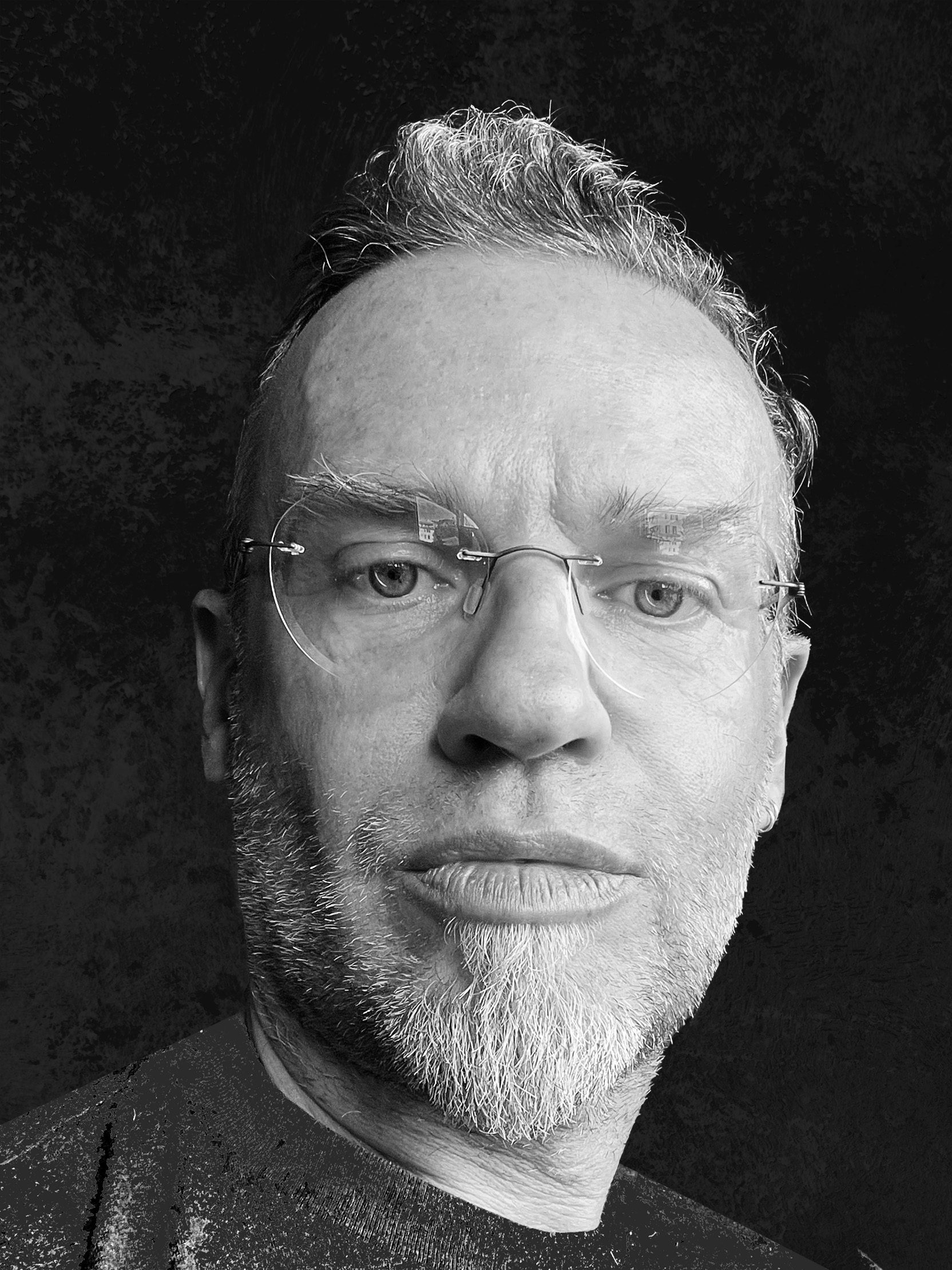 a closeup portrait of a man with short tousled hair and a beard wearing glasses the image is rendered in black and white highlighting the facial features against a dark background digital production A close-up portrait of a man with short, tousled hair and a beard, wearing glasses. The image is rendered in black and white, highlighting the facial features against a dark background.