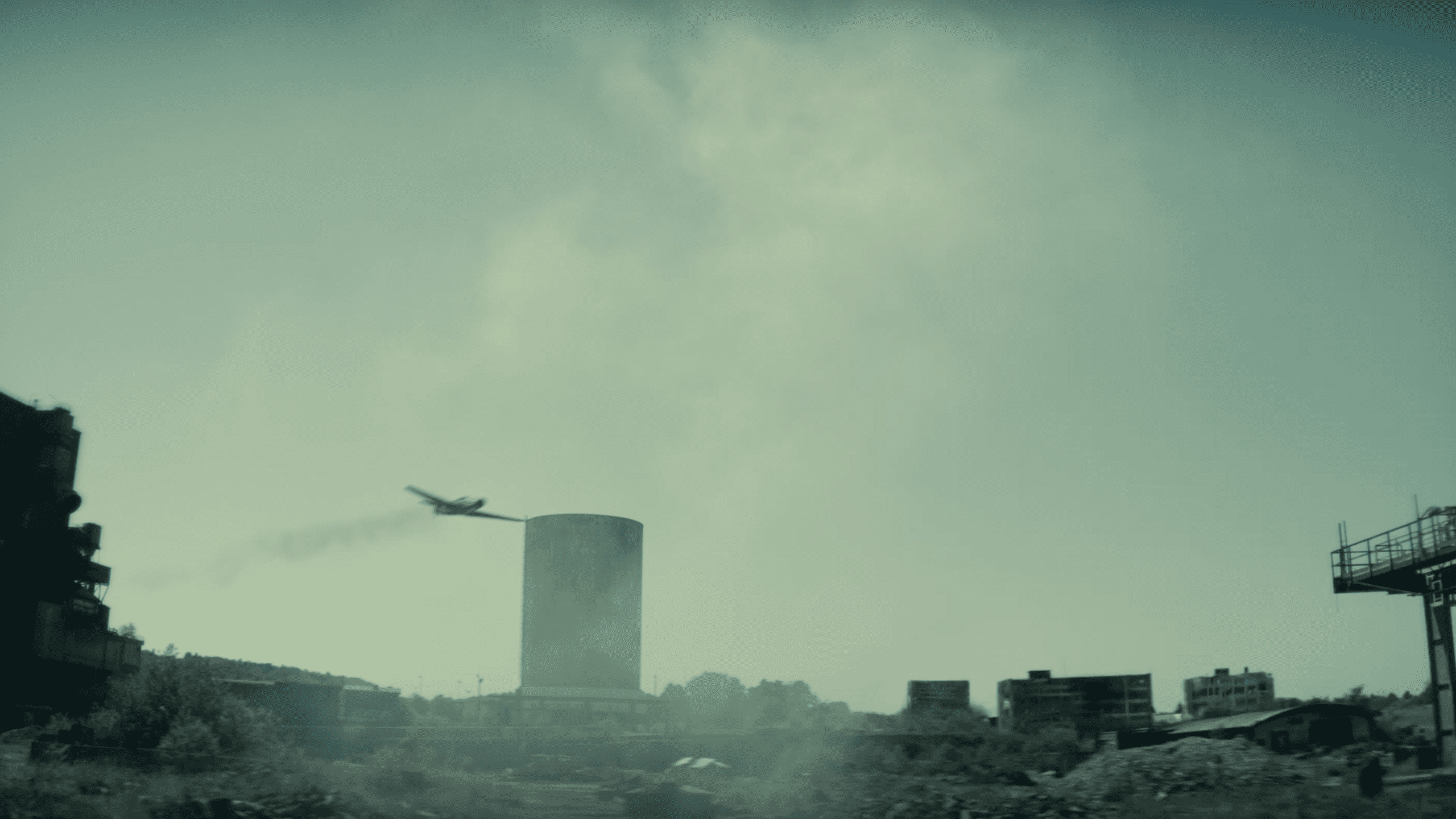 a small airplane flies above an industrial area with a large cylindrical structure and buildings in the background the scene is shrouded in a foggy muted atmosphere conveying an eerie desolate setting digital production A small airplane flies above an industrial area with a large cylindrical structure and buildings in the background. The scene is shrouded in a foggy, muted atmosphere, conveying an eerie, desolate setting.