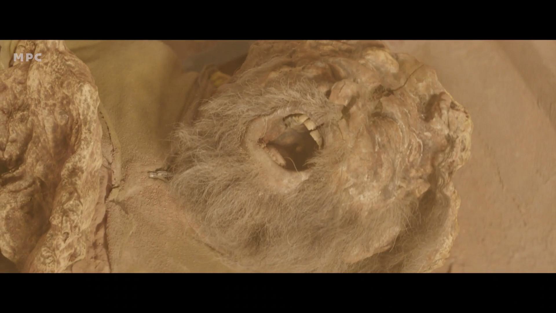 an ancient mummified figure with a grimace showing a white beard and exposed teeth lies in a sandy environment the figure is partially covered in a grainy texture emphasizing its age and deterioration digital production An ancient, mummified figure with a grimace, showing a white beard and exposed teeth, lies in a sandy environment. The figure is partially covered in a grainy texture, emphasizing its age and deterioration.