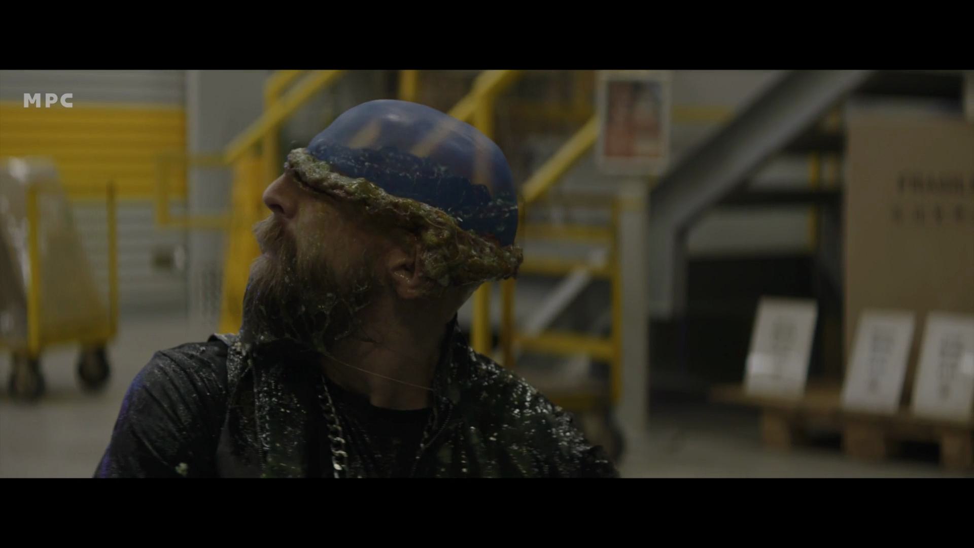 a man with a long beard and a blue painted helmet adorned with what appears to be seaweed looking upwards in a warehouse the surroundings include yellow industrial railings and cardboard boxes digital production A man with a long beard and a blue painted helmet, adorned with what appears to be seaweed, looking upwards in a warehouse. The surroundings include yellow industrial railings and cardboard boxes.