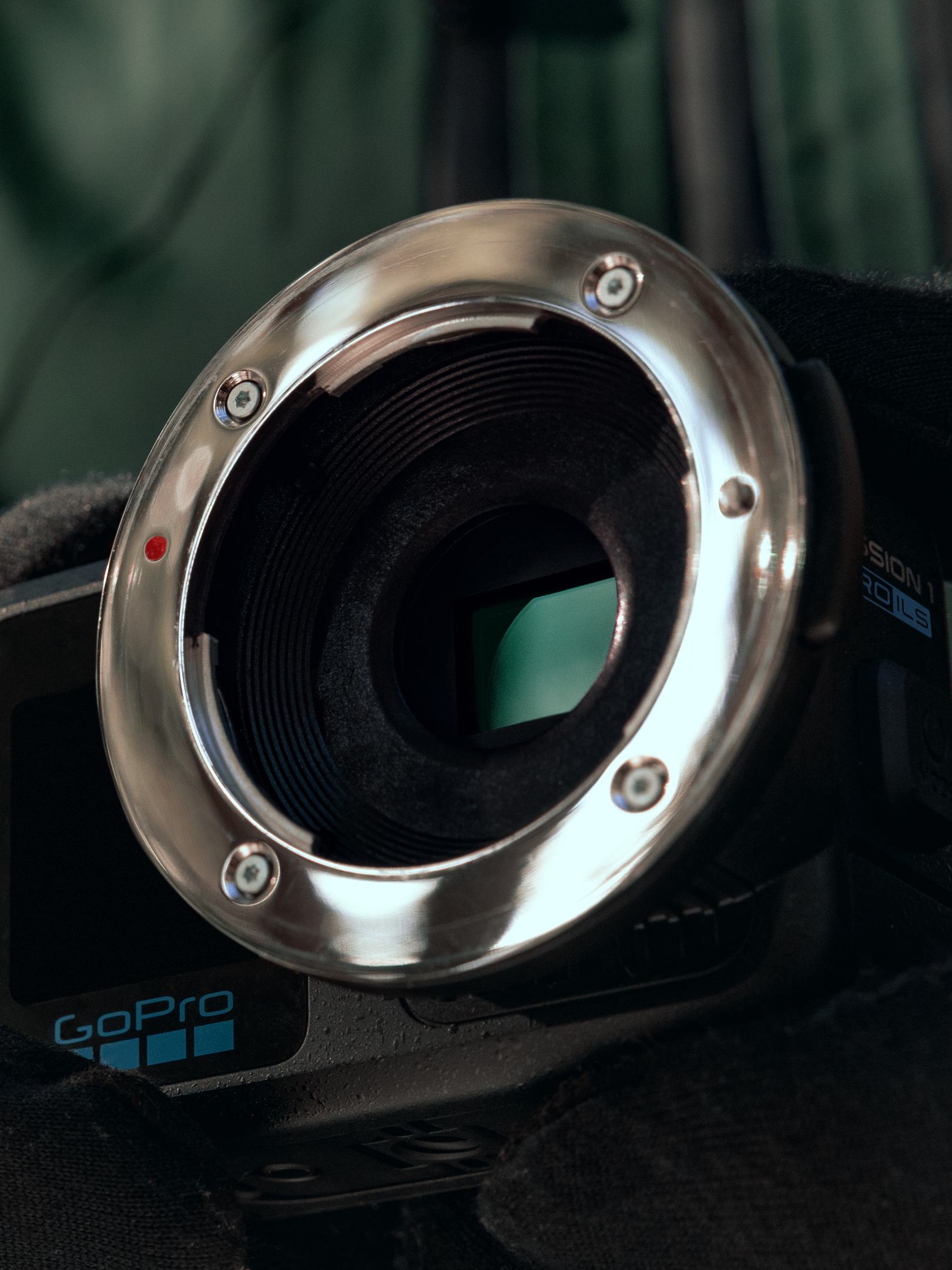 a closeup view of a gopro camera lens showcasing its shiny metallic rim and intricately designed inner grooves the lens exhibits a polished surface with screws visible indicating a robust construction a subtle hint of green fabric in the background adds depth to the scene digital production A close-up view of a GoPro camera lens, showcasing its shiny metallic rim and intricately designed inner grooves. The lens exhibits a polished surface with screws visible, indicating a robust construction. A subtle hint of green fabric in the background adds depth to the scene.